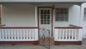 Una casa con fachada blanca, puerta roja y portón de metal.