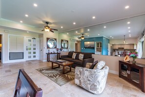 A spacious living room with a sofa, coffee table, and a patterned armchair. A ceiling fan and recessed lighting are visible.