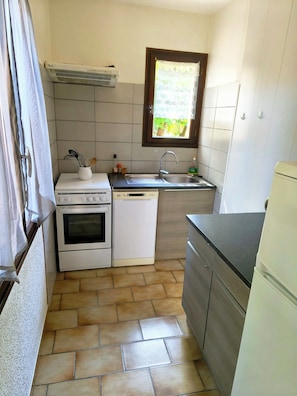 Eine kompakte Küche mit Herd, Backofen, Geschirrspüler, Spüle und einem Fenster über der Spüle.