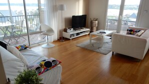 A modern living room with a sofa, a coffee table, a TV, and a balcony with a view of the water. - Apartment with harbor and sea view in Perros Guirec (Perros-Guirec)