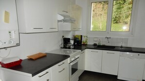 A kitchen with white cabinets, a black countertop, a coffee maker, and a window with a view of trees. - Apartment with harbor and sea view in Perros Guirec (Perros-Guirec)