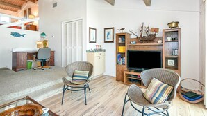 Un salon chaleureux avec un plafond en bois, un téléviseur, des fauteuils en osier et une bibliothèque.