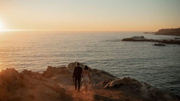Una pareja camina sobre un sendero rocoso junto al mar durante el atardecer.
