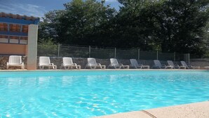 A swimming pool with lounge chairs along the edge, a stone wall, and a building with a blue roof in the background.