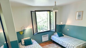 A room with two beds, a window, a wall-mounted light, and a ceiling fan.