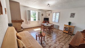 A living room with a sofa, a dining table with chairs, a TV, and a ceiling fan.