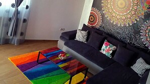 A modern living room with a dark sofa, colorful rug, and a large decorative tapestry.