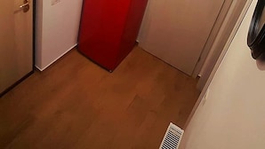 A compact room with a red refrigerator, a wooden door, a white wall, and a hanging light fixture.