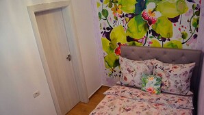A bedroom with a bed, a nightstand, a floral-patterned wall, and a door.