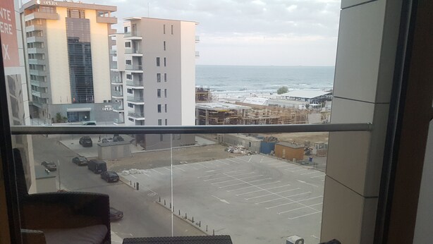 A balcony with wicker furniture overlooking a parking lot and a view of the sea.