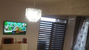 A living room with a television, a cabinet, and a window with blinds.
