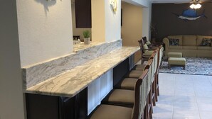 A modern kitchen with a marble countertop, a built-in island with bar stools, and decorative fish wall art. - Tropical pool home close to the beach, never floods, high and dry  (Seminole)