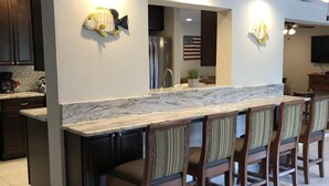 A modern kitchen with a marble countertop, dark wooden cabinets, and a bar area with striped chairs. - Tropical pool home close to the beach, never floods, high and dry  (Seminole)