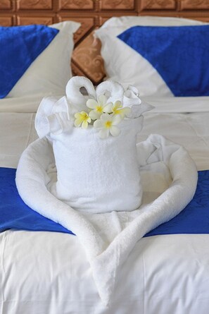 A neatly made bed with a white towel and flowers, blue pillows, and a wooden headboard. - The President Hotel (Nadi)