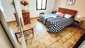 A bedroom with a bed, a chair, a nightstand, a lamp, a window, and a wall-mounted picture.