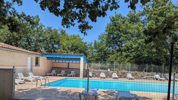 A swimming pool with lounge chairs, a covered seating area, and a stone wall.