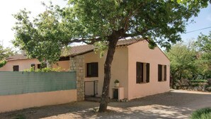 A single-story house with a stone wall, a small porch, and a gravel driveway.