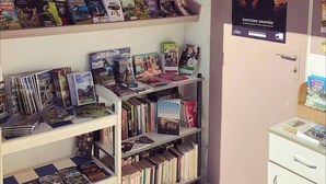 A bookstore with multiple shelves of books, a poster on the wall, and a small desk with a chair.