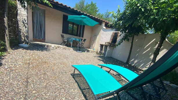 Un'area patio con tavolo e sedie, un ombrellone verde e due poltrone da relax.