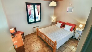 A bedroom with a wooden bed, a nightstand, a desk, a window with curtains, and a ceiling light.