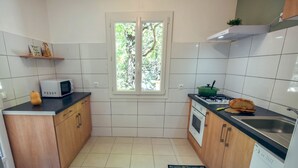 A compact kitchen with white tiles, a microwave, a stove, and a sink.