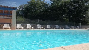 A swimming pool with lounge chairs along the edge, a stone wall, and a building with a blue roof in the background.
