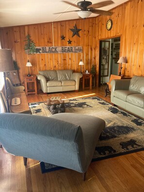 A cozy living room with a wooden wall, a ceiling fan, a couch, a coffee table, and a rug.