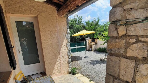 Un espacio al aire libre techado con un muro de piedra, una puerta, una mesa con sillas amarillas y un paraguas amarillo.
