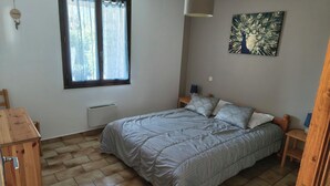 Un dormitorio con cama, ventana con cortinas, una obra de arte en la pared, mesita de noche con lámpara y radiador.