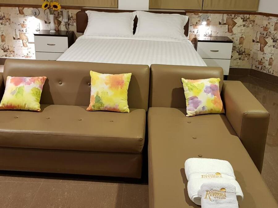 A hotel room with a bed, a brown sofa, and a small table with a towel.