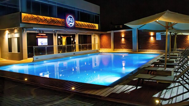 A swimming pool area with lounge chairs and umbrellas, a neon sign, and a brick wall.