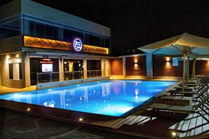 A swimming pool area with lounge chairs and umbrellas, a neon sign, and a brick wall.