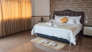 A hotel room with a large bed, a nightstand, a lamp, a decorative wall, and a window with curtains.