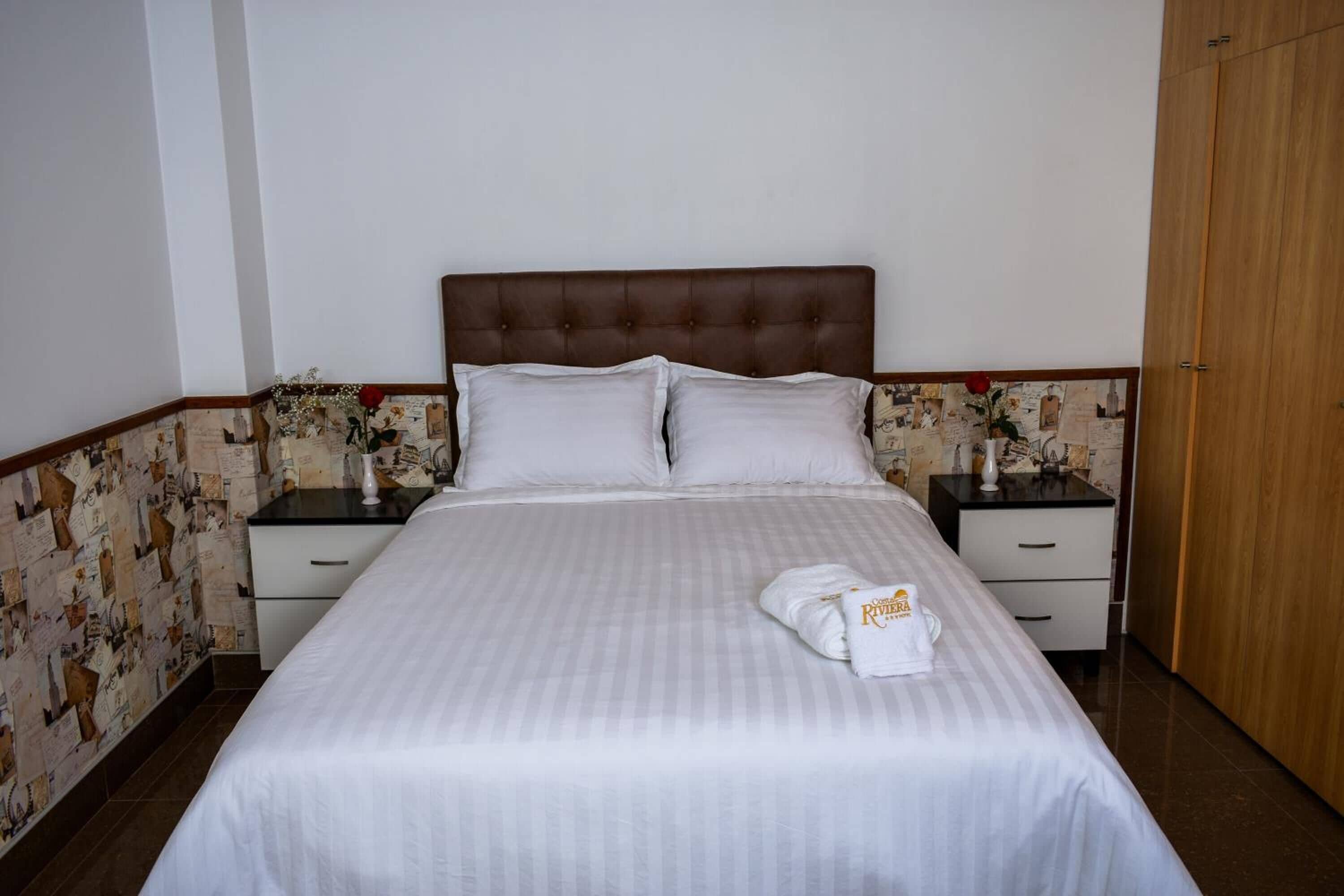 Una cama bien hecha con sábanas blancas, dos mesitas de noche con lámparas y un armario de madera.