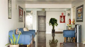 A hotel lobby with a blue sofa, a potted plant, a fire extinguisher, and a refrigerator.