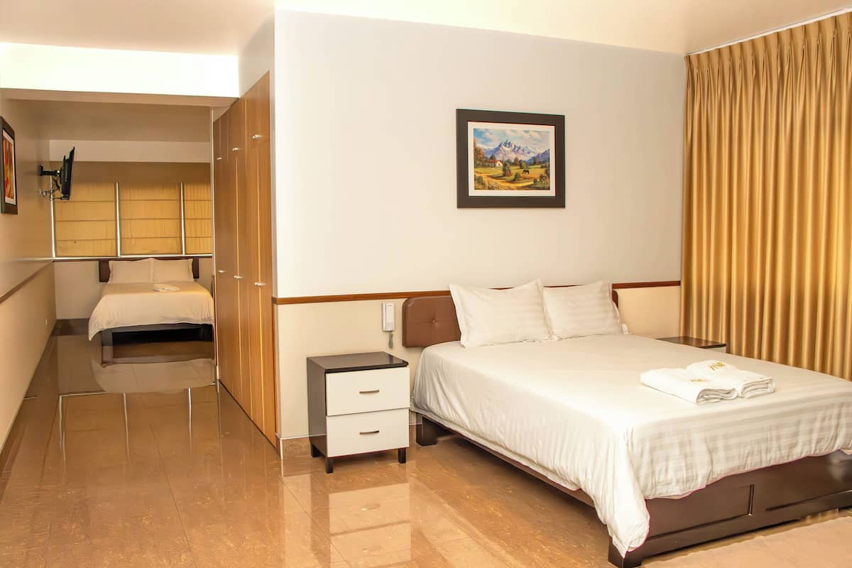 A hotel room with a bed, bedside tables, a small desk, a chair, a wardrobe, and a painting on the wall.
