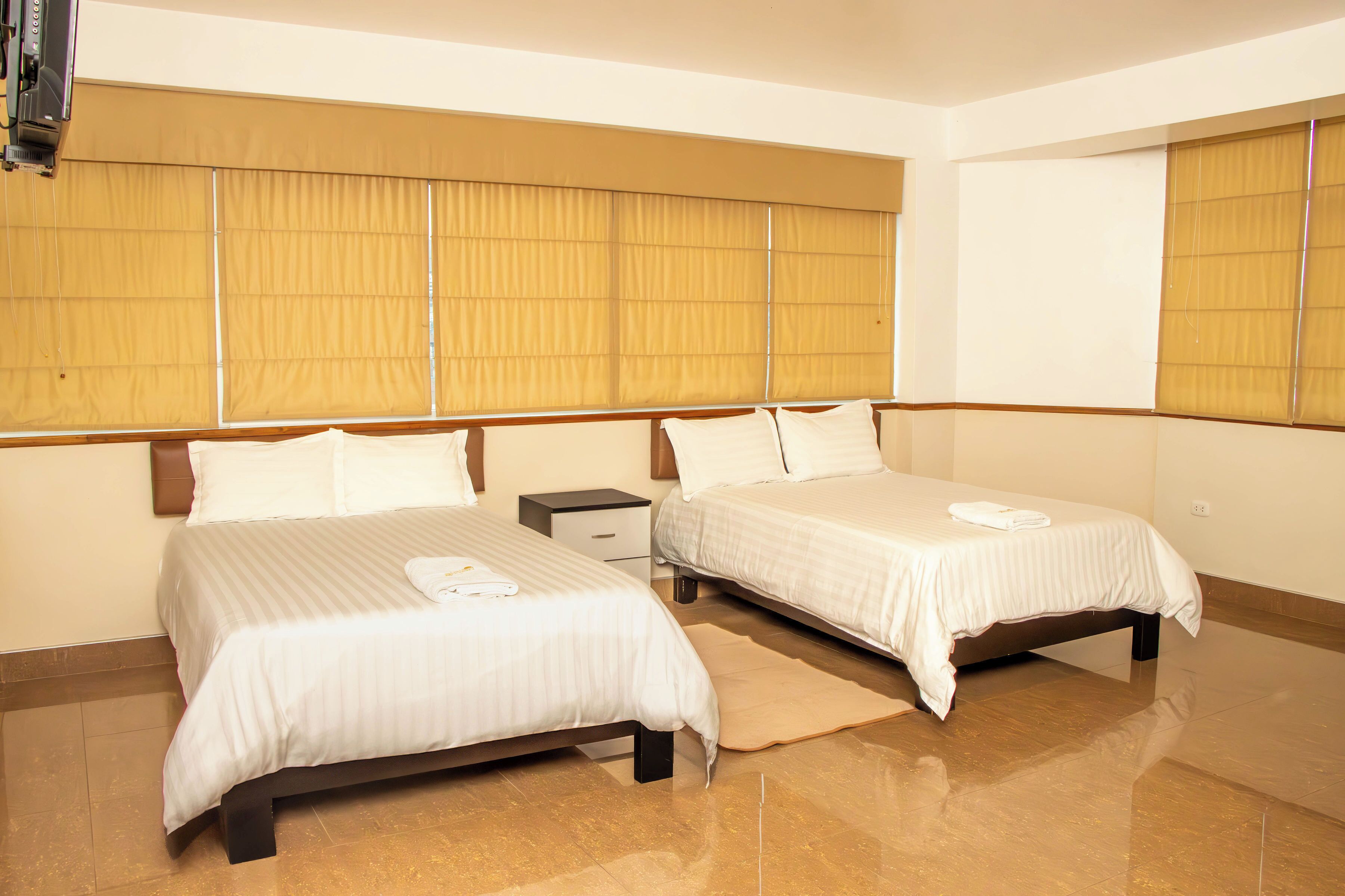 Habitación de hotel con dos camas, una mesita de noche y un ventanal con persianas.