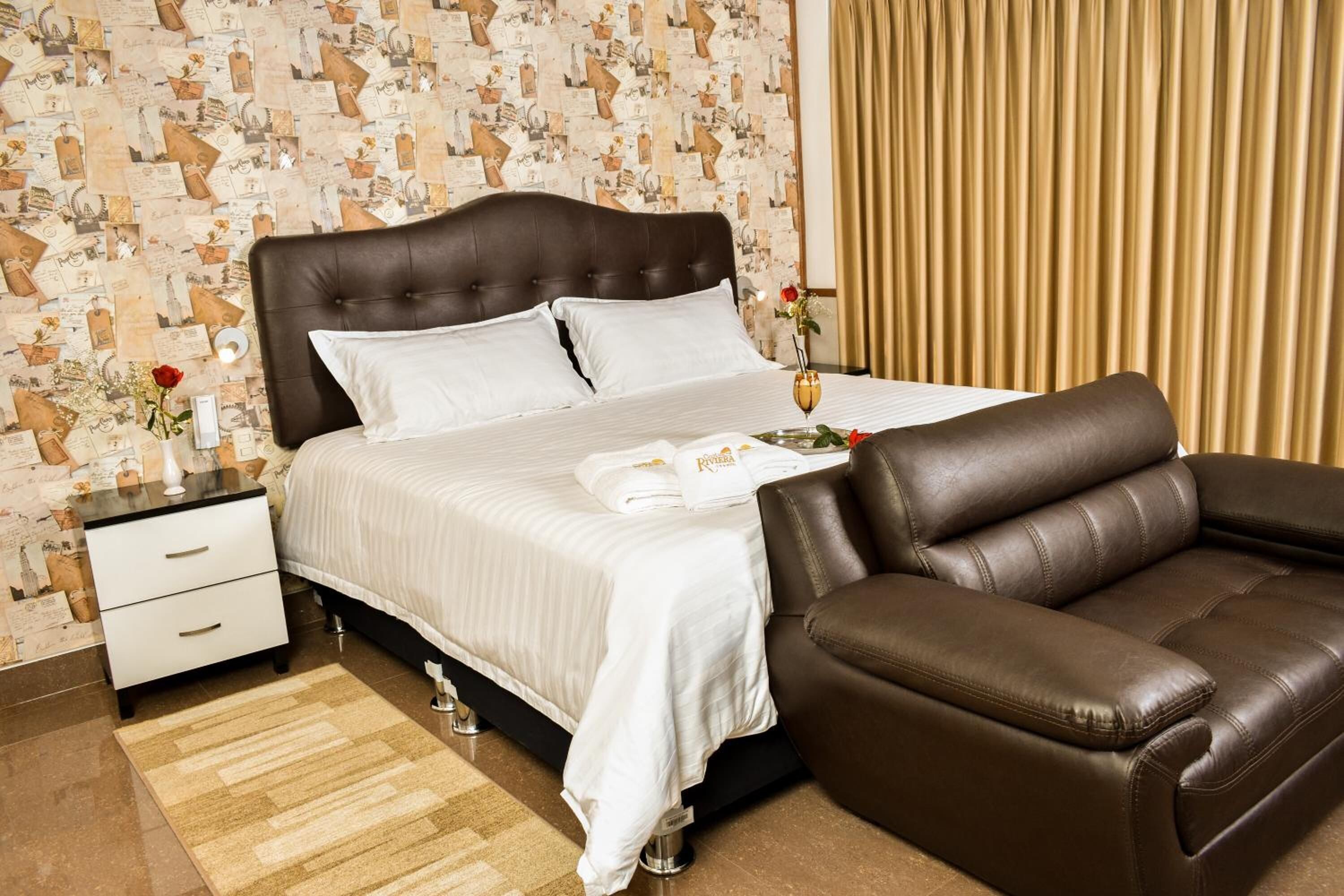 A bedroom with a bed, a brown leather sofa, a nightstand, and a wall with a patterned wallpaper.