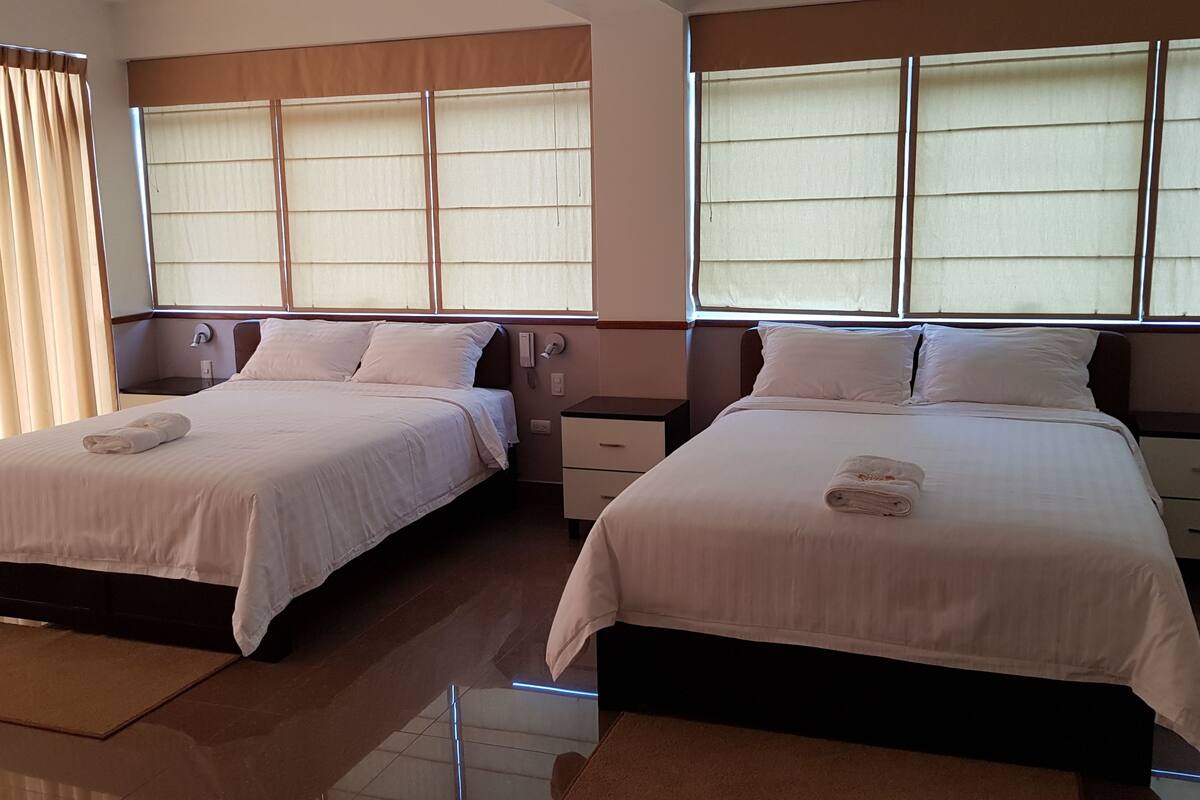 A hotel room with two beds, each with a pillow and a folded towel. There are bedside tables with drawers and a mirror above the beds.