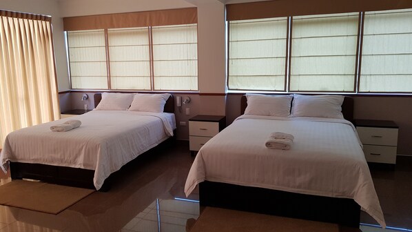 A hotel room with two beds, each with a pillow and a folded towel. There are bedside tables with drawers and a mirror above the beds.