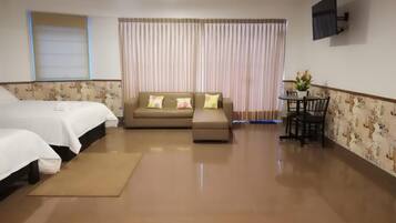 A hotel room with two beds, a sofa, a small table with chairs, and a large window with curtains.