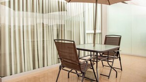 A meeting room with a glass table and chairs, a large umbrella, and a view through a patterned curtain.