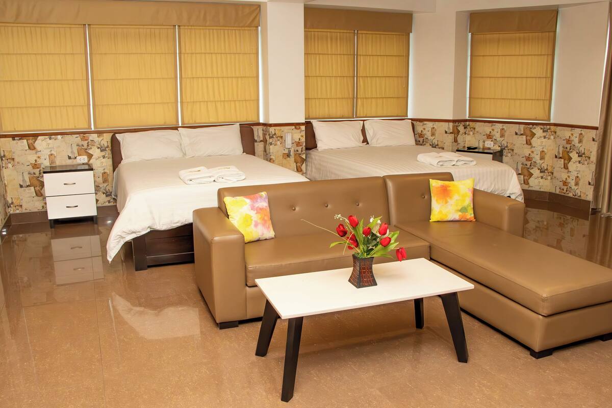 A hotel room with a large bed, a sofa, a small table, and a nightstand.