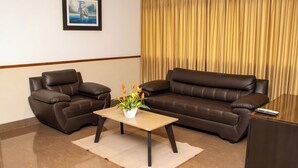 A living room with two brown leather sofas, a wooden coffee table with a plant, a framed picture on the wall, and a curtain.