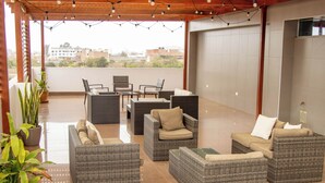 A covered outdoor seating area with wicker furniture, potted plants, and string lights.