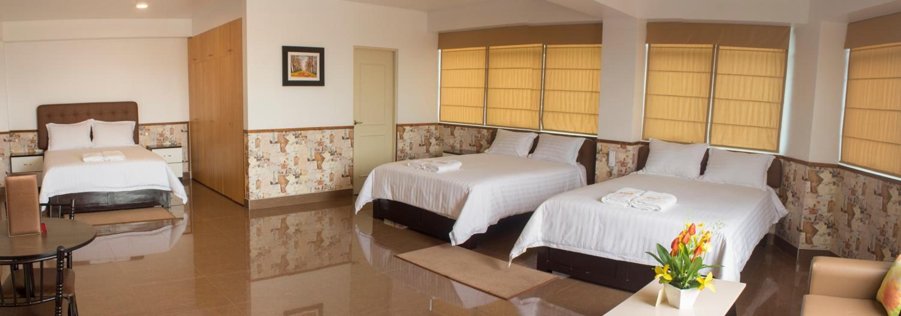 A hotel room with two beds, a sitting area, and a large window with blinds.