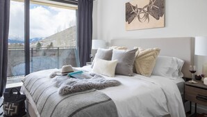 A bedroom with a large bed, a view of mountains, a painting on the wall, and a handbag on the floor. - Outpost: One Town Hill 507 - Base of Snow King Mtn (Jackson)