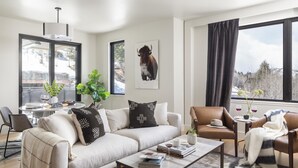 A modern living room with a sofa, coffee table, and chairs, a large window with a view of a snowy landscape, and a mounted artwork of a bison. - Outpost: One Town Hill 507 - Base of Snow King Mtn (Jackson)