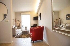 Un salon moderne avec un fauteuil rouge, un canapé et une table basse. Un grand miroir est accroché au mur, et un téléviseur est fixé au-dessus.