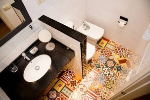 Une salle de bain avec un plan de toilette noir, un lavabo blanc, un miroir rond, des toilettes et un carrelage à motifs.
